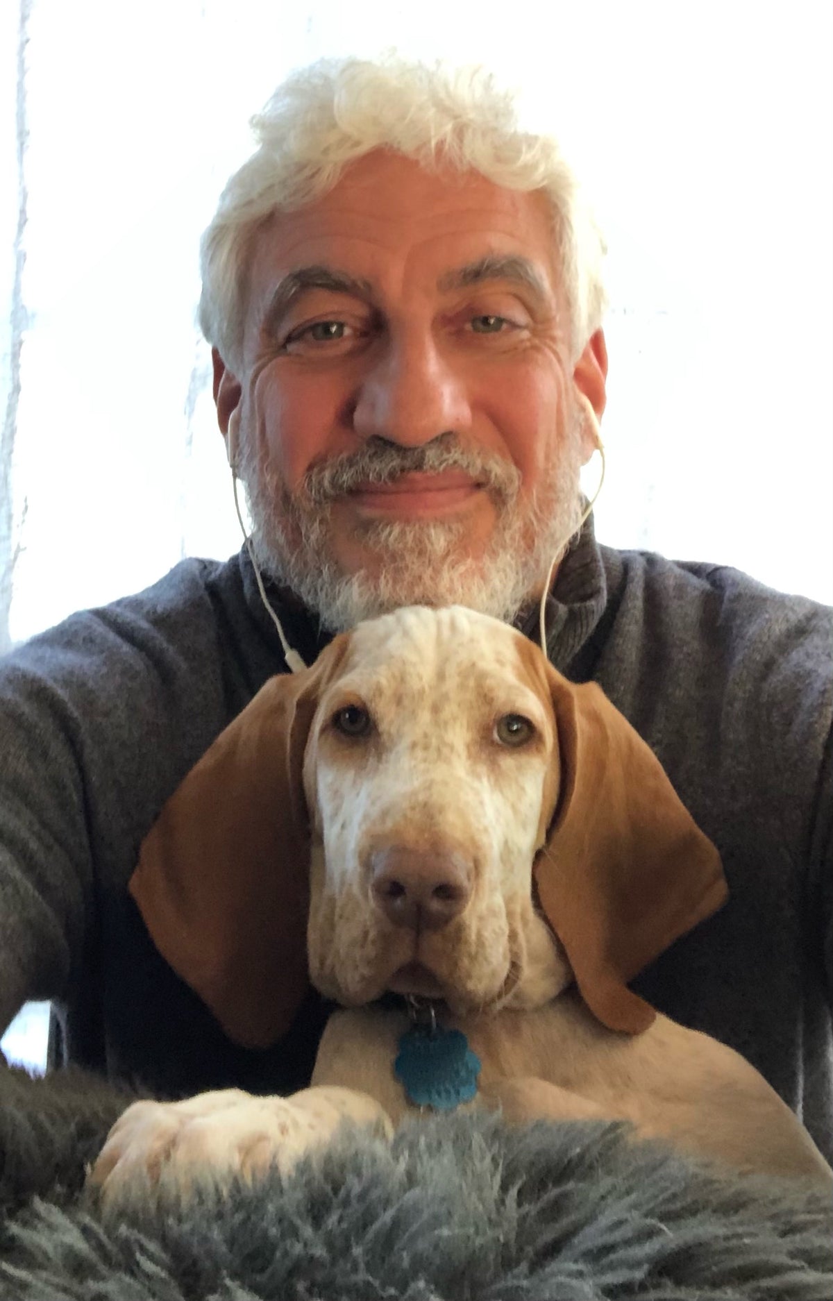 A man holding a young brown-and-white hound puppy indoors.